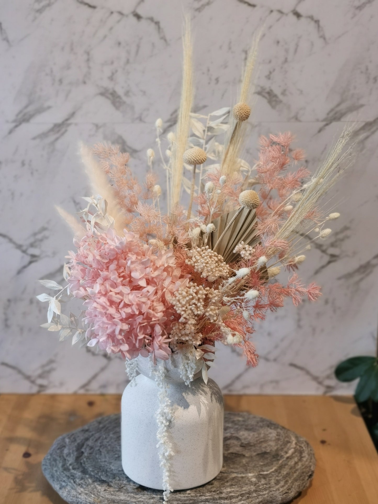 This pink arrangement will suit any display with its white and pink colours.
This gorgeous arrangement in an antique looking pot is made from a wide range of beautiful preserved & dried flowers which consists of: Hydrangea, Rice flowers, Seaholly, Ruscus, Bunnytale, Billy button and more. It comes with white ceramic pot.Height 48cm | Width 30cm