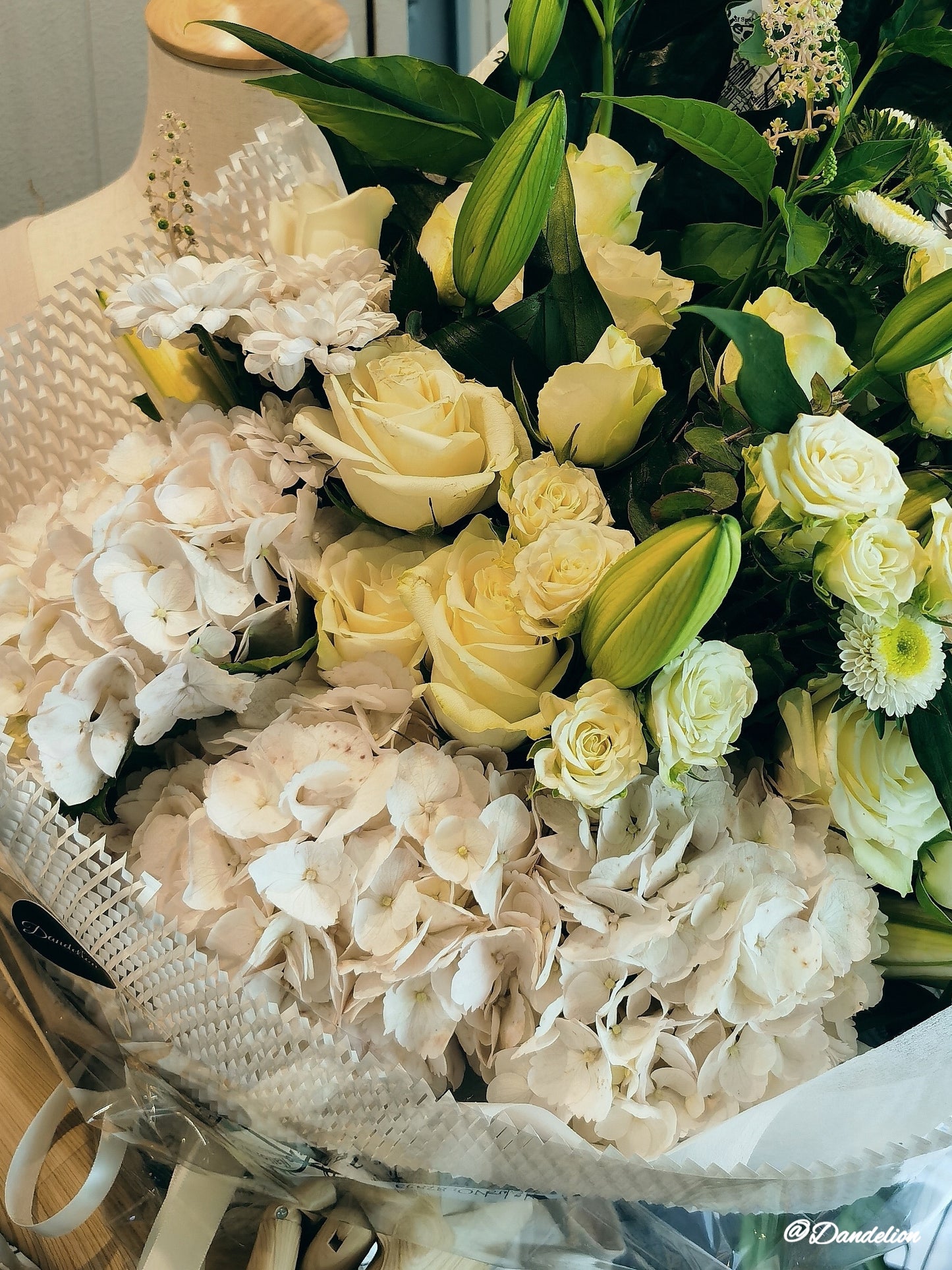 A stunning floral arrangement featuring a mix of white roses, lilies and other seasonal fresh flowers with accompanying green foliage.