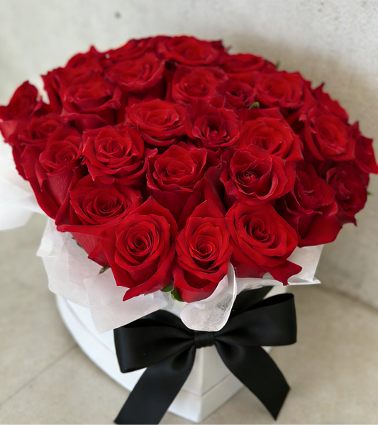 Lush dome of velvety red roses in a white box with a black bow