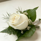 A white rose boutonniere floral arrangement with green leaves and white rose. White wrist corsage and buttonhole bundle for weddings and formal events