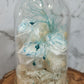A handmade everlasting preserved white flower dome cloche arrangement under a floral archway, displayed on a wooden stand. The dome is approximately 19cm in height and 10cm in diameter.