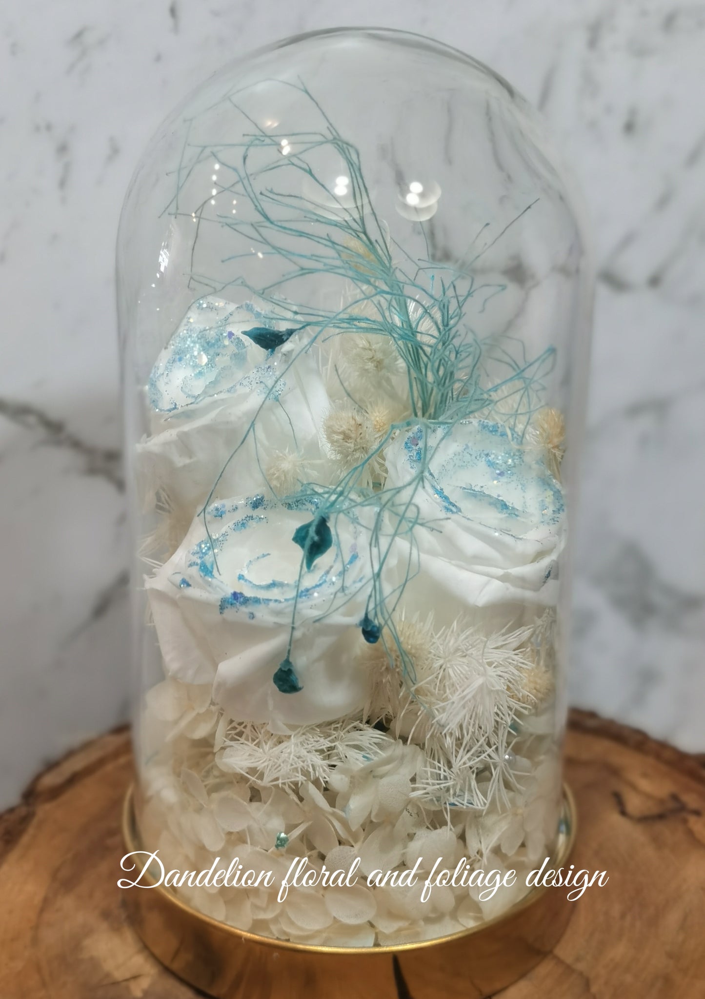 A handmade everlasting preserved white flower dome cloche arrangement under a floral archway, displayed on a wooden stand. The dome is approximately 19cm in height and 10cm in diameter.