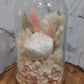 A handmade everlasting preserved white and pink flower dome cloche arrangement under a floral archway, displayed on a wooden stand. The dome is approximately 19cm in height and 10cm in diameter.