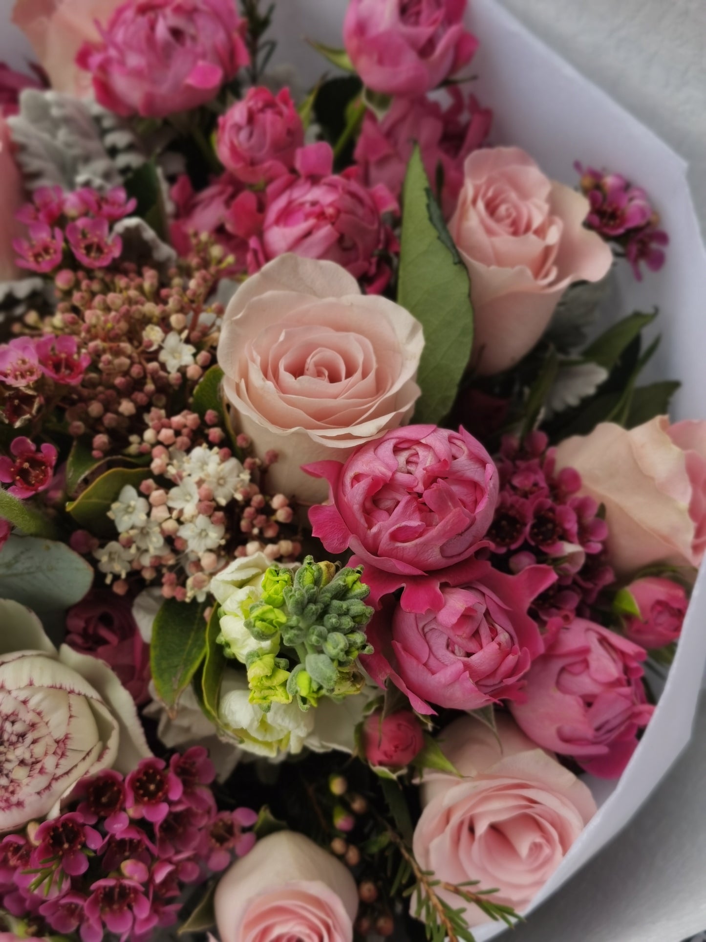 A mixed flower bouquet with white, pink roses, and soft mint green colors, wrapped and placed on a wooden bench.