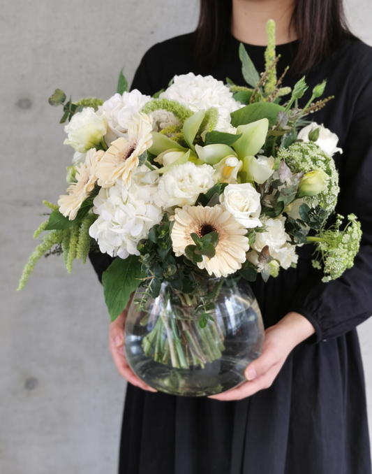 This lush, creamy-white arrangement blends hydrangeas, gerberas, and roses with fresh green accents in vase. It’s a soft, elegant statement of gentle warmth and timeless grace—perfect for gifting or bringing a peaceful, natural glow to any space