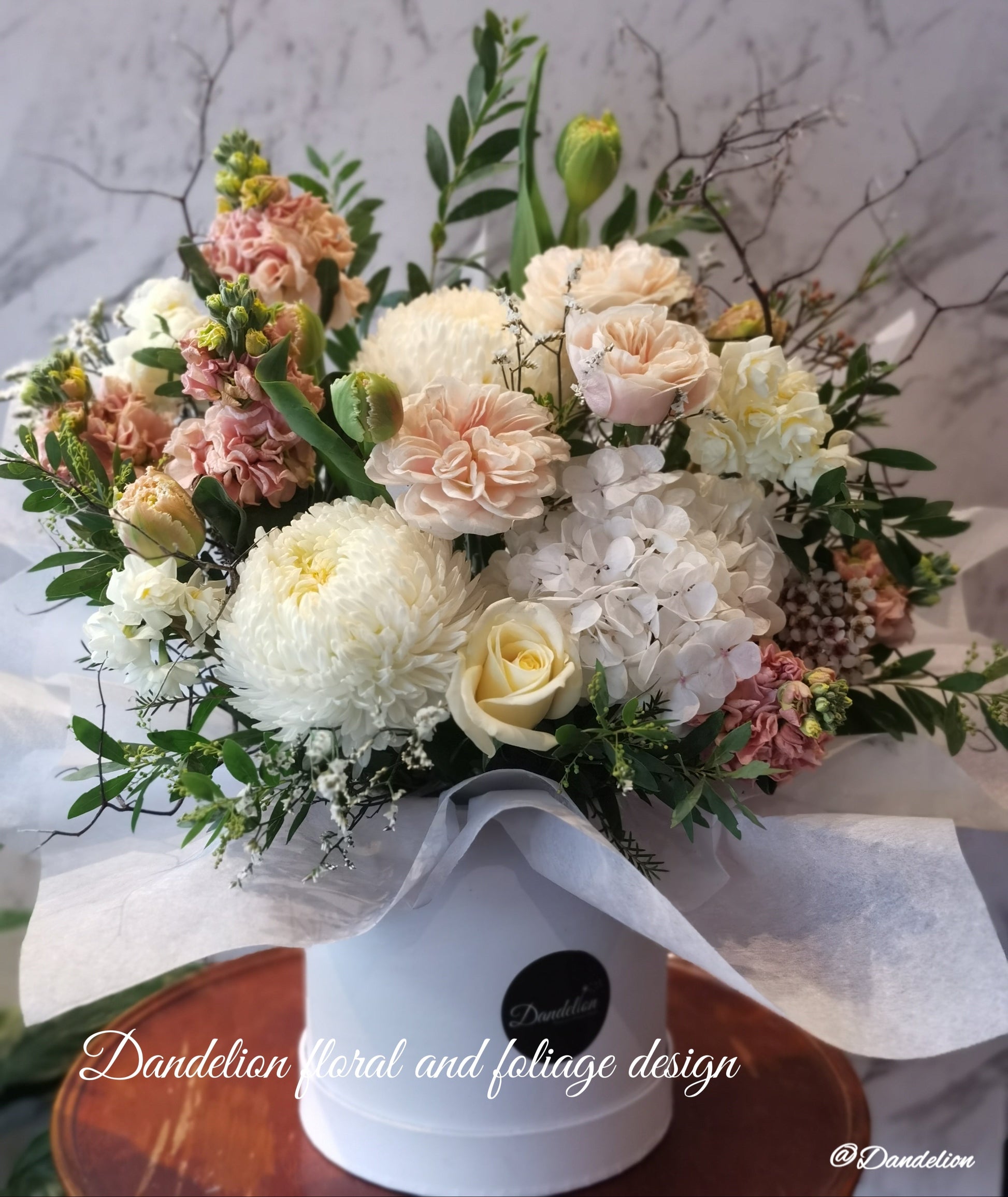 Mixed seasonal light pink flower arrangement including roses and lilies in a white flat hat box.
