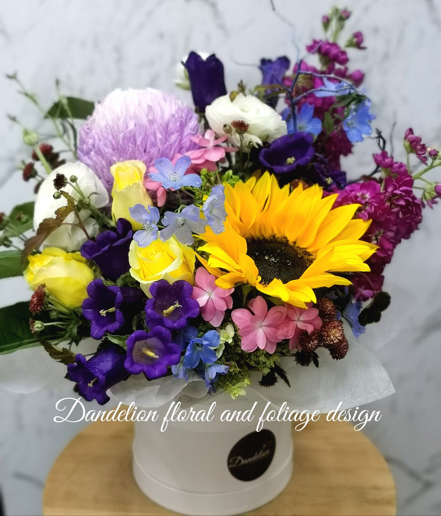 Vibrant orange and yellow seasonal flower display artfully arranged in a white flat hat box.