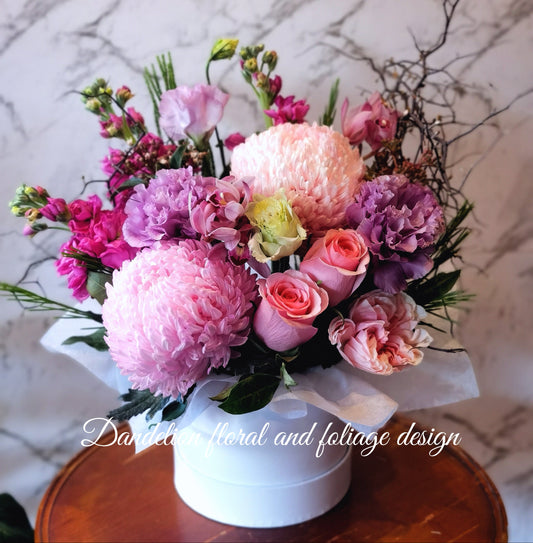 Mixed seasonal pink flower arrangement including roses and lilies in a white flat hat box.