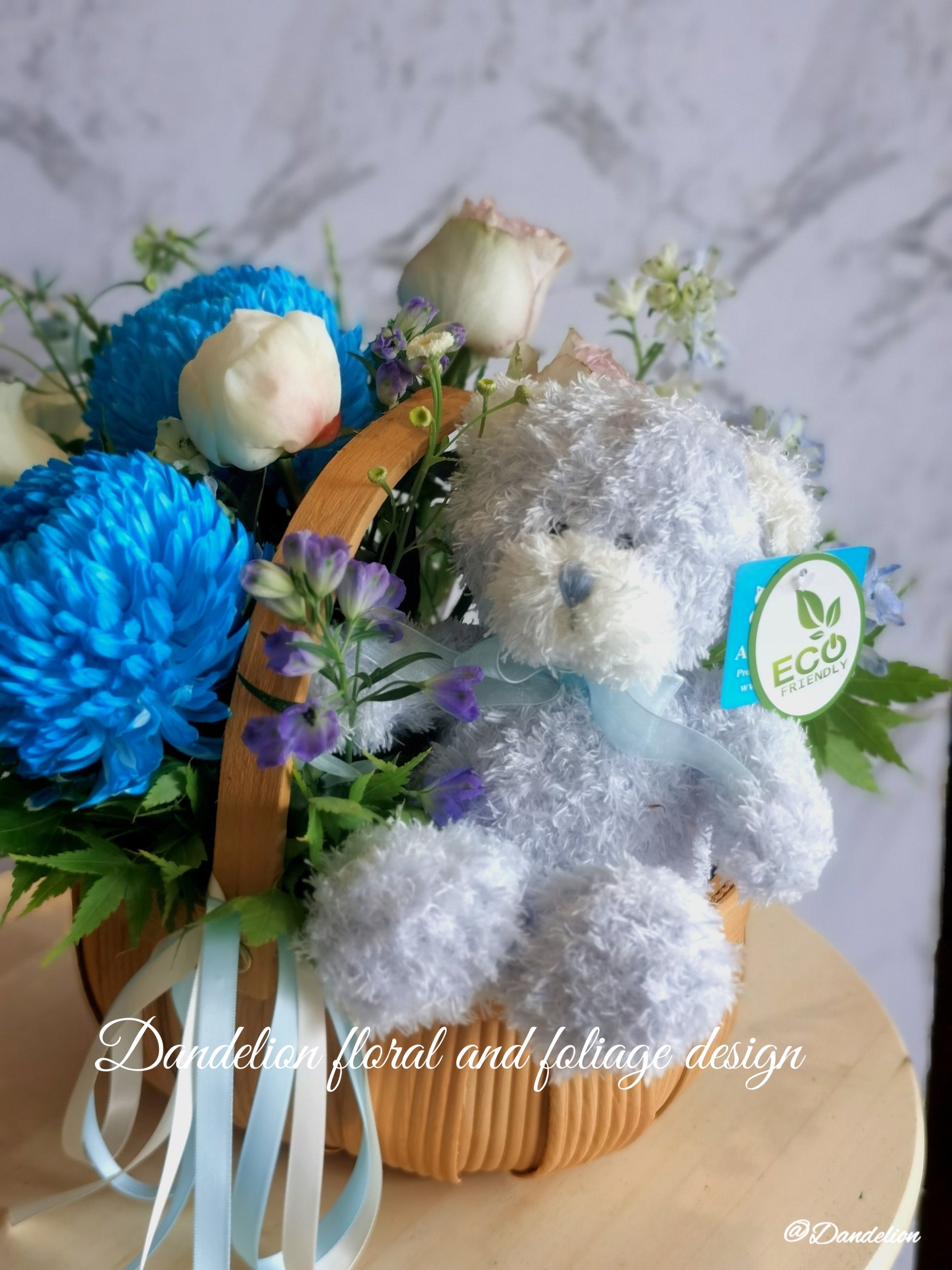 Congratulate new parents or beautify the home with a gorgeous palette of white florals with a touch of blue. For added joy this arrangement includes a fluffy teddy bear. The gift includes seasonal white, blue and green flowers in a basket.