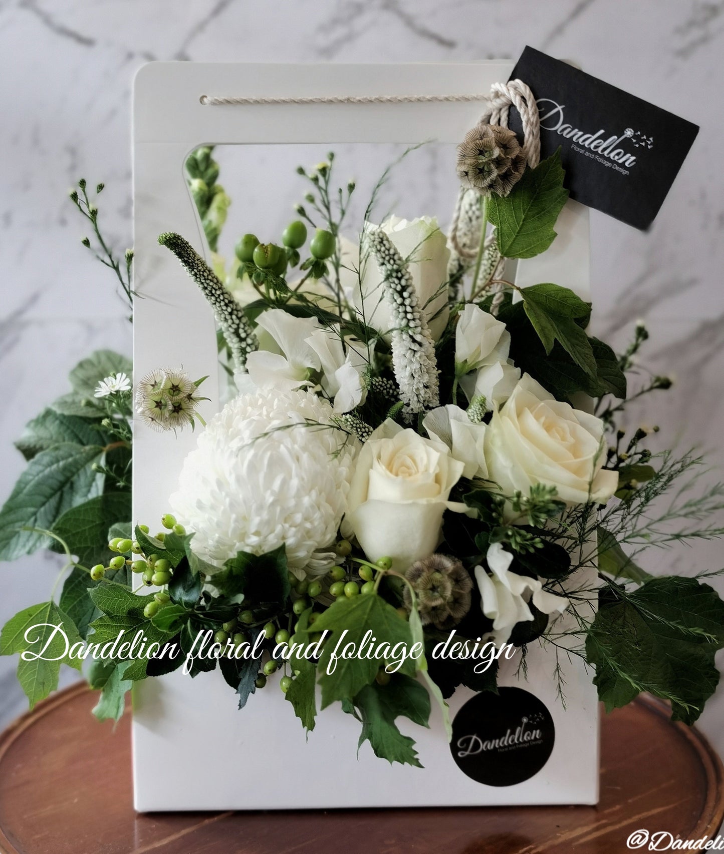 A floral carry box arrangement with a variety of flowers including white roses, and green foliage, presented in a rectangular white box.