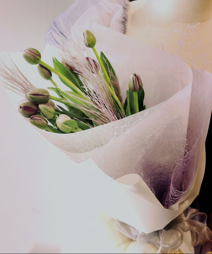 A bouquet of deep purple tulips wrapped in champagne and lilac paper with silvery eucalyptus leaves, which symbolizes endless love and gratitude