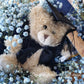 A bouquet of blue flowers with a teddy bear wearing a graduation cap and gown, surrounded by dark paper and a blue bow. 
Celebrate the achievement of your loved ones with beautiful graduation flowers. Find the perfect bouquet or arrangement to congratulate the graduate on their special day.
