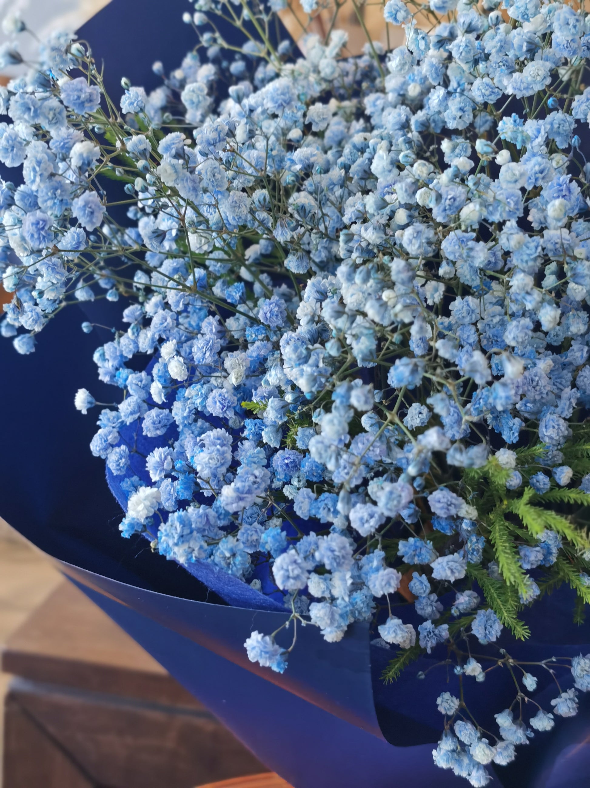 A bouquet of blue flowers with a teddy bear wearing a graduation cap and gown, surrounded by dark paper and a blue bow. 
Celebrate the achievement of your loved ones with beautiful graduation flowers. Find the perfect bouquet or arrangement to congratulate the graduate on their special day.