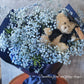 A bouquet of blue flowers with a teddy bear wearing a graduation cap and gown, surrounded by dark paper and a blue bow. 
Celebrate the achievement of your loved ones with beautiful graduation flowers. Find the perfect bouquet or arrangement to congratulate the graduate on their special day.