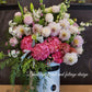 A large pink hat box flower arrangement featuring a variety of beautiful and premium flowers, displayed in a shopfront setting. 