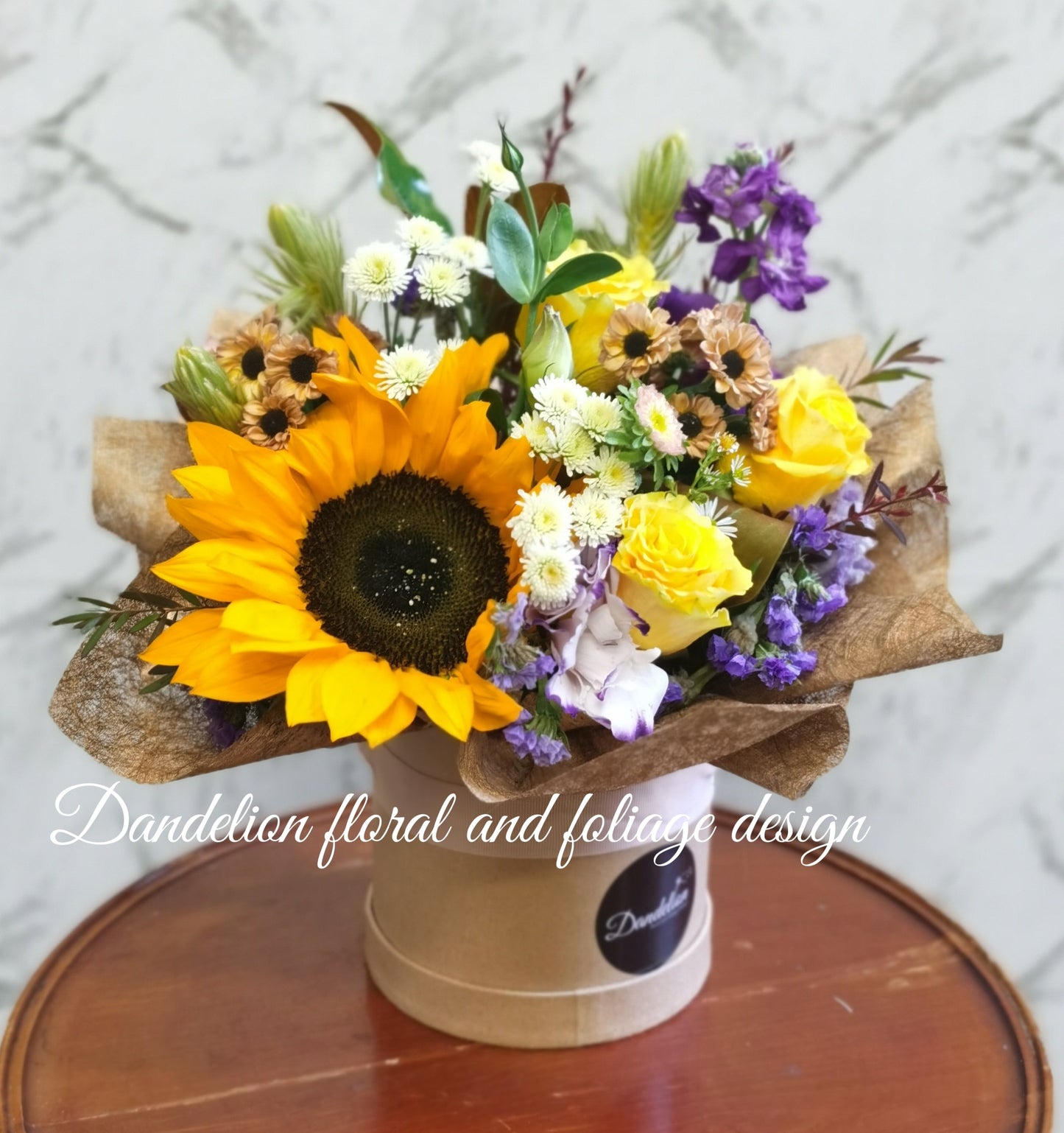 Medium arrangement of sunflowers and other yellow/orange flowers in hat box