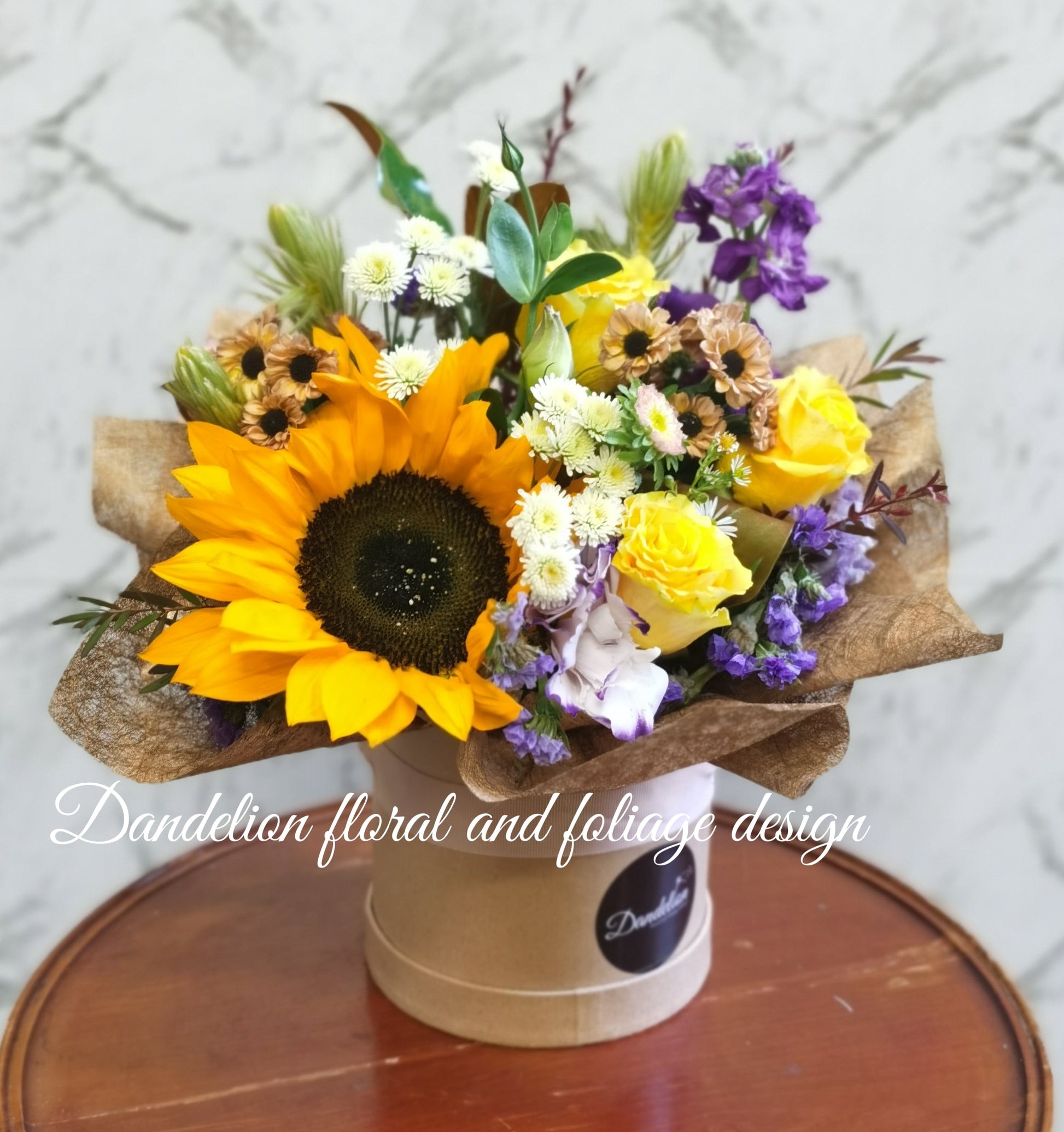 Medium arrangement of sunflowers and other yellow/orange flowers in hat box