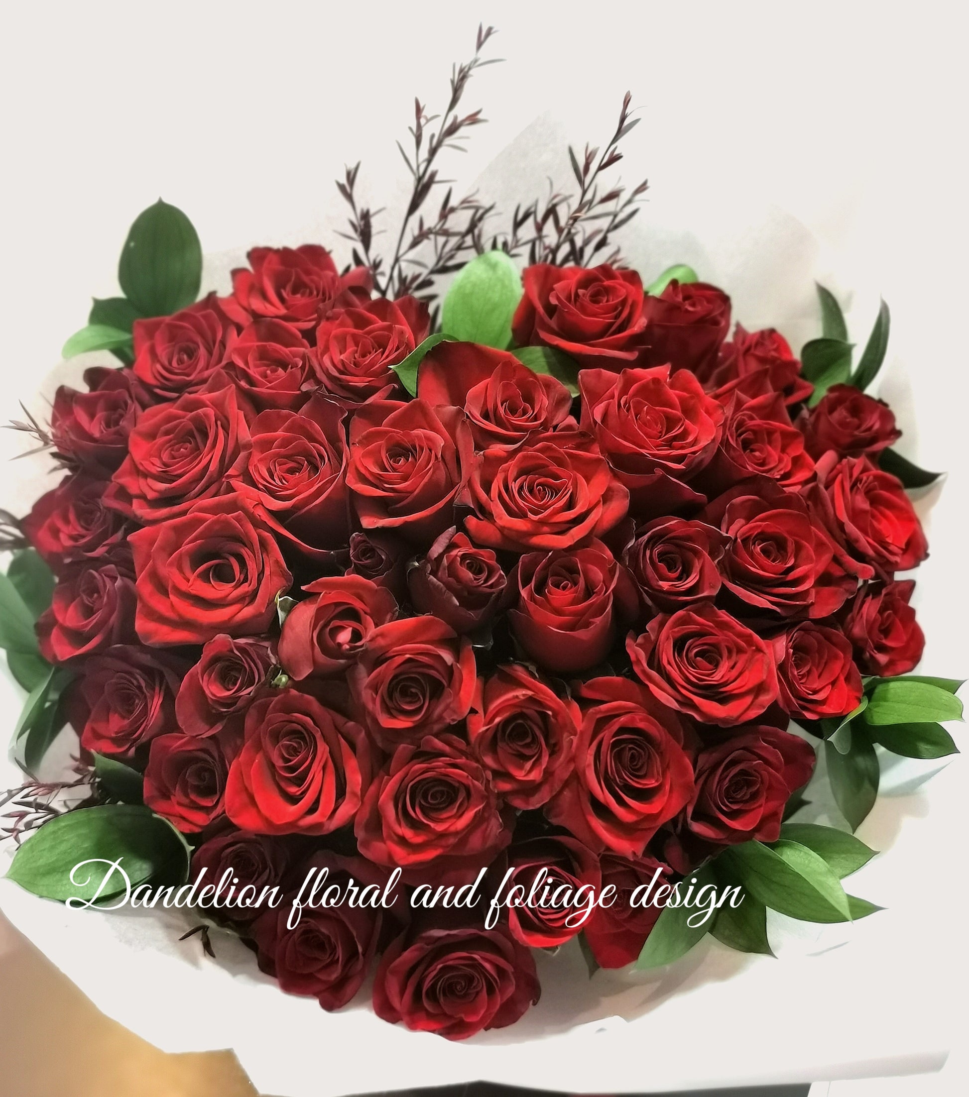 A heart-shaped bouquet of red roses arranged to represent a beating heart, wrapped in white paper with foliage accents. This exquisite heart-shaped rose bouquet is a masterpiece of unique design, crafted to symbolize eternal love. Each rose is meticulously arranged to form a perfect heart, making it a stunning and unforgettable gift for any romantic occasion. Rose length is 40cm or 50cm.