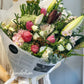 Soft pastel flower bouquet featuring roses and lilies in light pink and cream tones, hand-wrapped