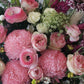 A round white hat box with a fresh flower arrangement consisting of pink, red and white flowers with green leaves.