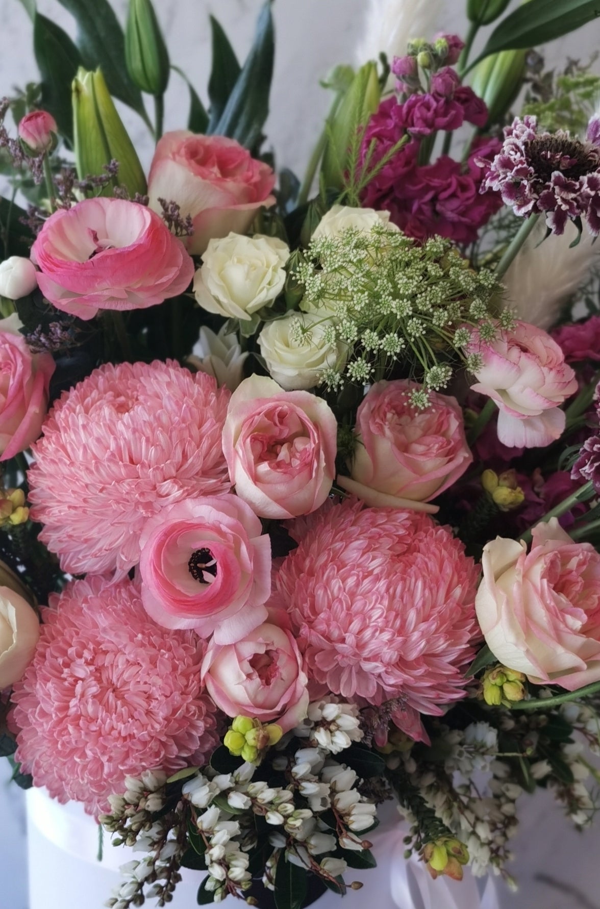 A round white hat box with a fresh flower arrangement consisting of pink, red and white flowers with green leaves.
