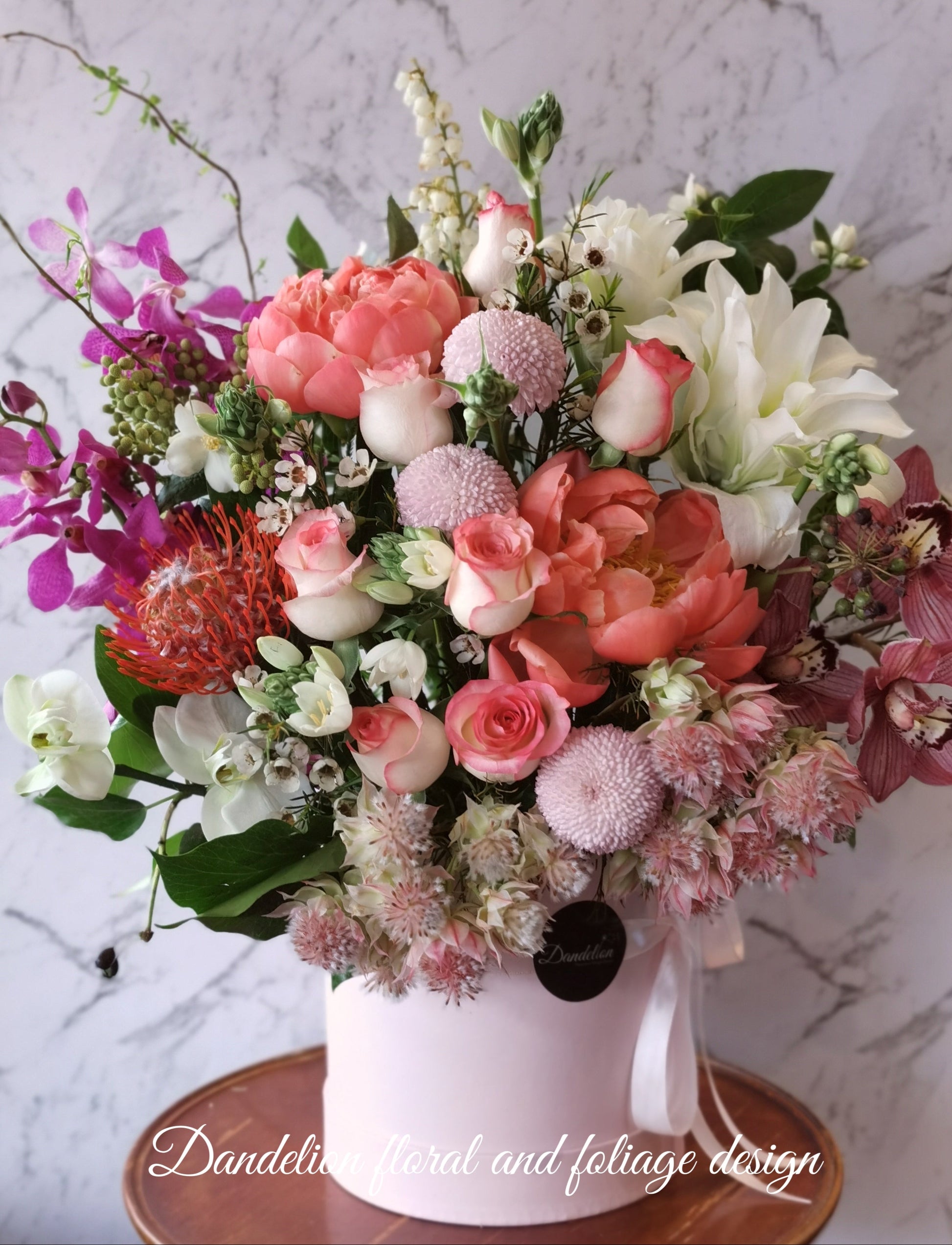 A floral arrangement featuring a variety of flowers including pink roses, orchids, and other plants in a hat box. Whether you're celebrating birthdays, anniversaries, weddings, or extending sympathy and support, our flowers and gifts are crafted to resonate with the unique emotions of each moment. Our commitment to quality ensures that every floral arrangement and gift is an embodiment of your care and consideration, destined to leave an impression.