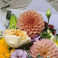Bouquet of flowers with a pink dahlia and other colorful blooms on a textured surface.