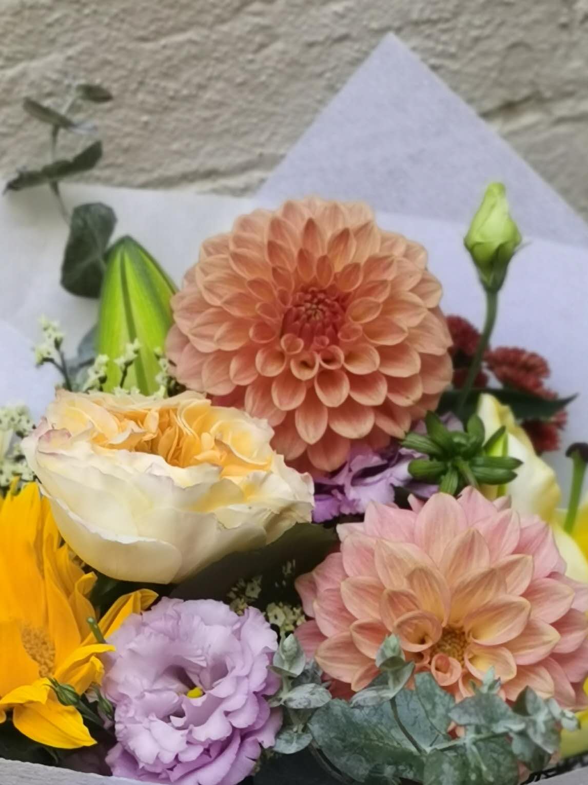 Bouquet of flowers with a pink dahlia and other colorful blooms on a textured surface.