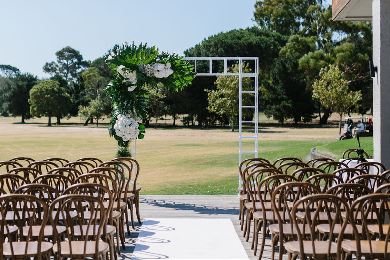 Wedding ceremony setup with floral arch and chairs on a grassy field.