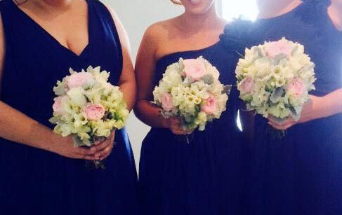 Three women in navy blue dresses holding floral bouquets indoors.