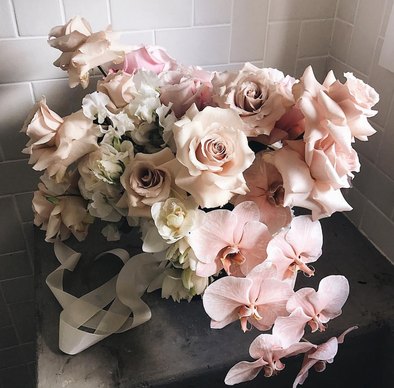 Floral arrangement with pink and white flowers on a dark surface against a tiled wall.