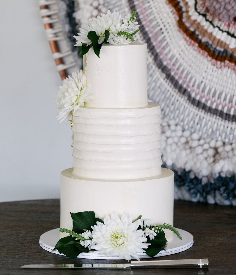 White wedding cake with floral decorations on a wooden table against a textured wall.