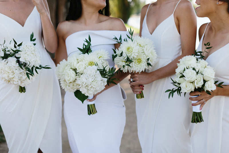 Four women in white dresses holding white bridal and bridesmaid bouquets.