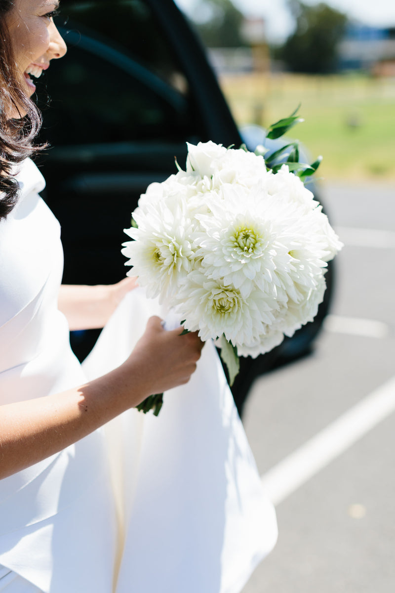 Woman in a white dress holding a bridal bouquet of white flowers outdoors for wedding