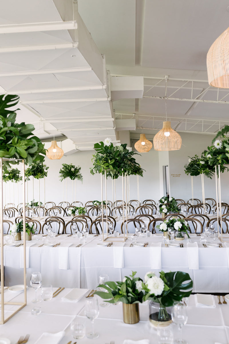 Decorated wedding space with tables, chairs, and white and green floral arrangements as table centrepieces.