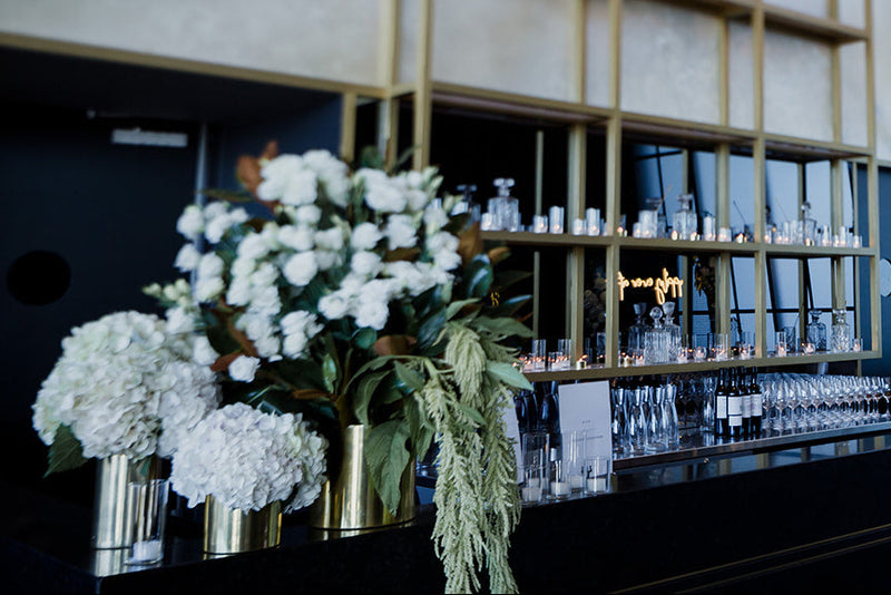 Modern bar interior with white and green floral arrangements and a large window.
