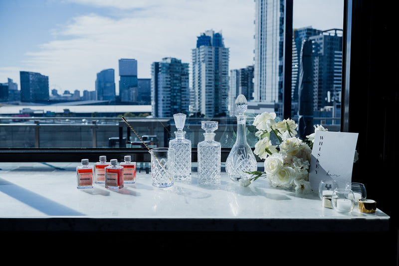 Table setup with bottles, glasses, and white flowers against a city skyline for wedding
