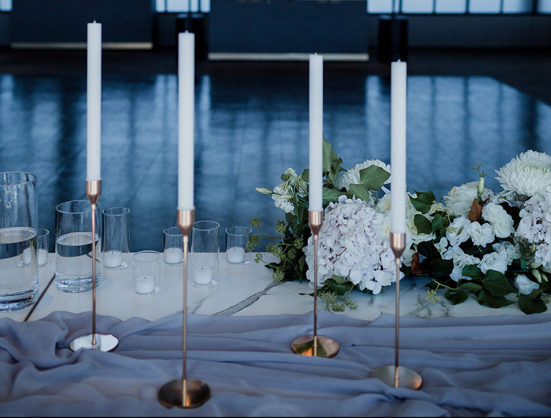 Decorative setup with candles,white and green flowers, and a large window in the background