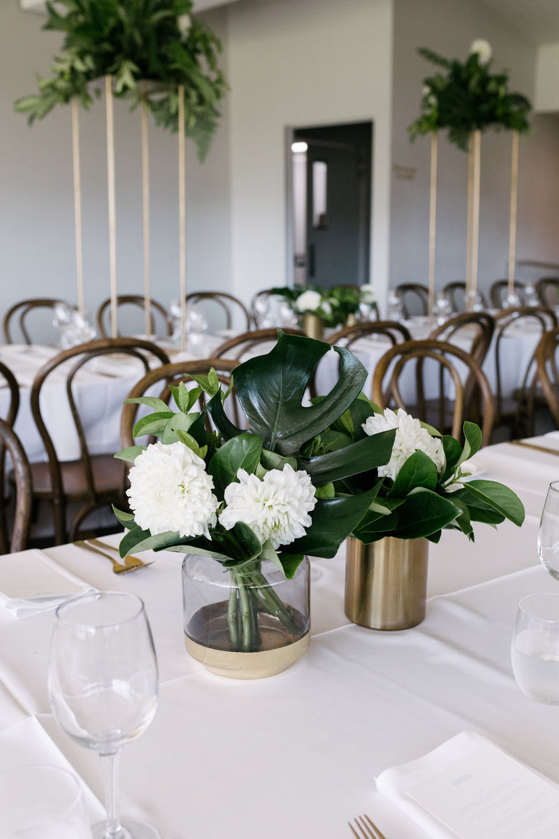 Decorative floral arrangements on a table with white tablecloth and wooden chairs in a room for wedding