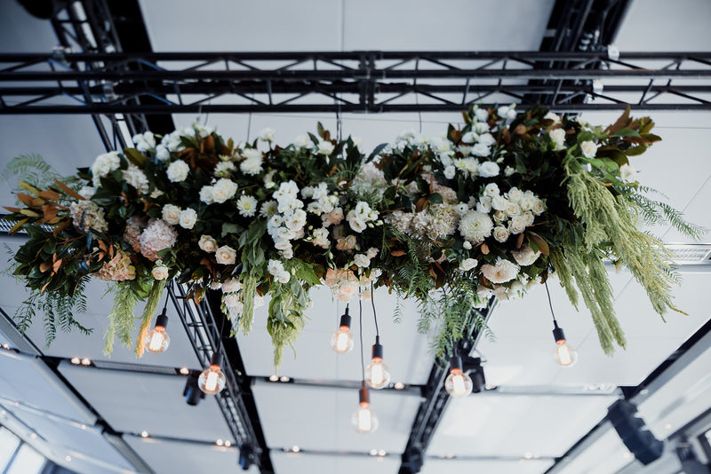 White and green floral arrangement hanging from the ceiling with decorative lights