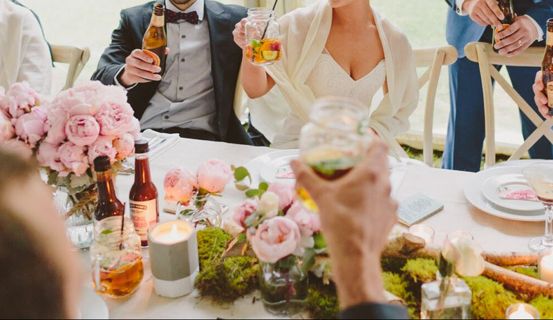 Group of people at a wedding reception with drinks and floral decorations.