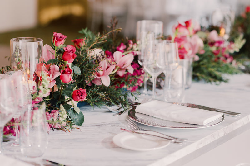 Elegant table setting with floral arrangements and cutlery on a white tablecloth.