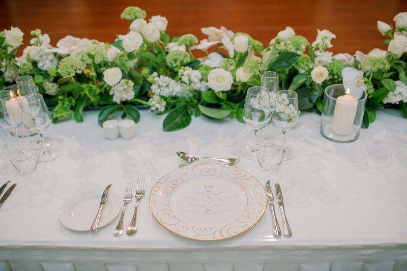 Elegant table setting with white flowers and roses, candles, and silverware on a white tablecloth.