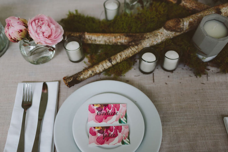 Table setting with floral centerpiece, candles, and name cards on a wooden table.