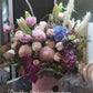 A round white hat box with a fresh flower arrangement consisting of pink, red and white flowers with green leaves.