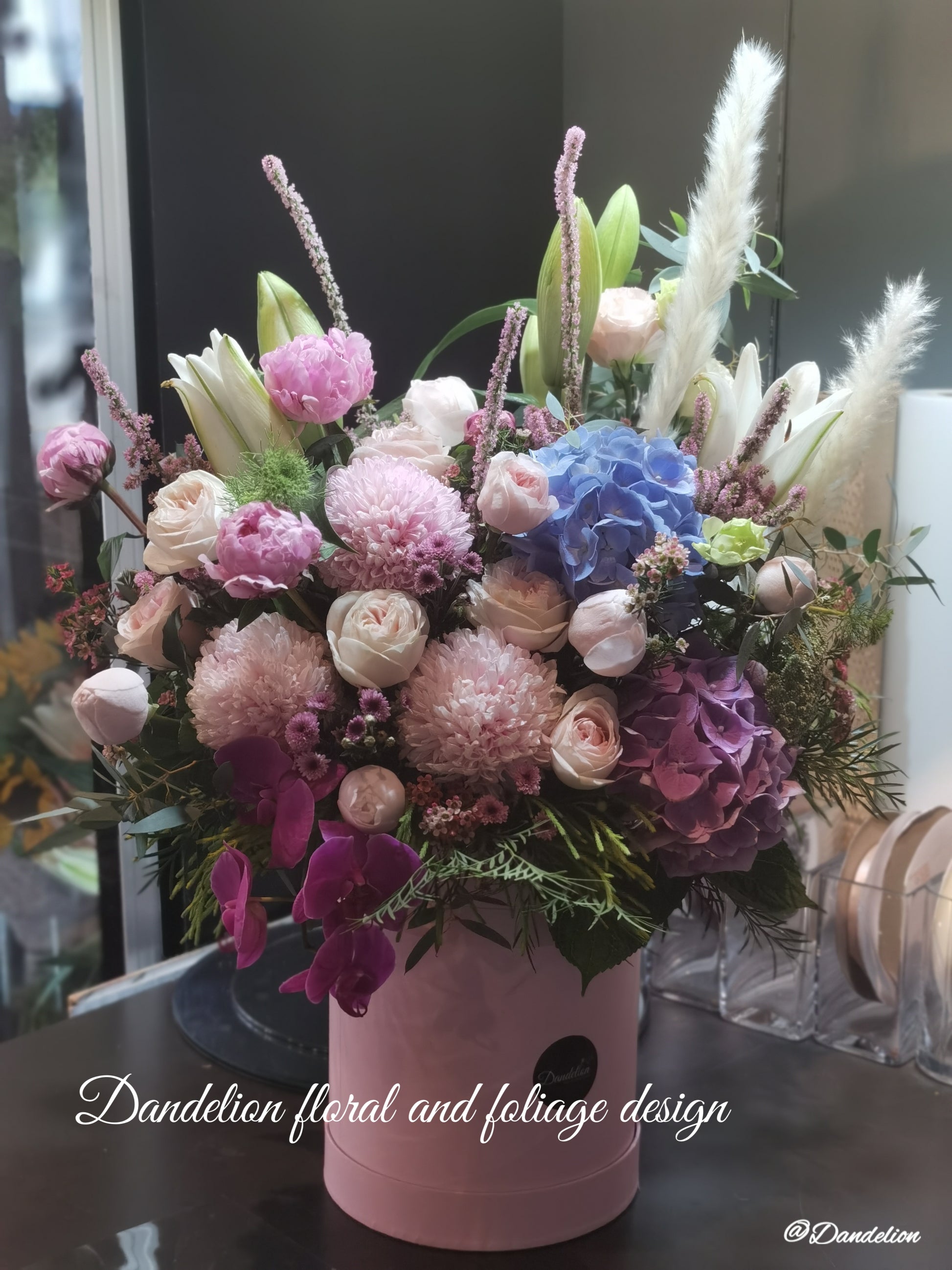 A round white hat box with a fresh flower arrangement consisting of pink, red and white flowers with green leaves.