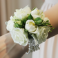 A wrist corsage featuring white flowers and green leaves for school formal, attached to a clear band.