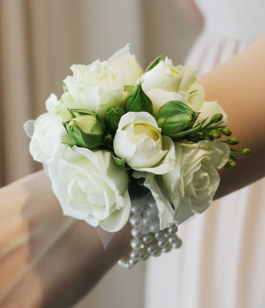 A wrist corsage featuring white flowers and green leaves for school formal, attached to a clear band.