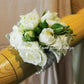 A wrist corsage featuring white flowers and green leaves, attached to a clear band.