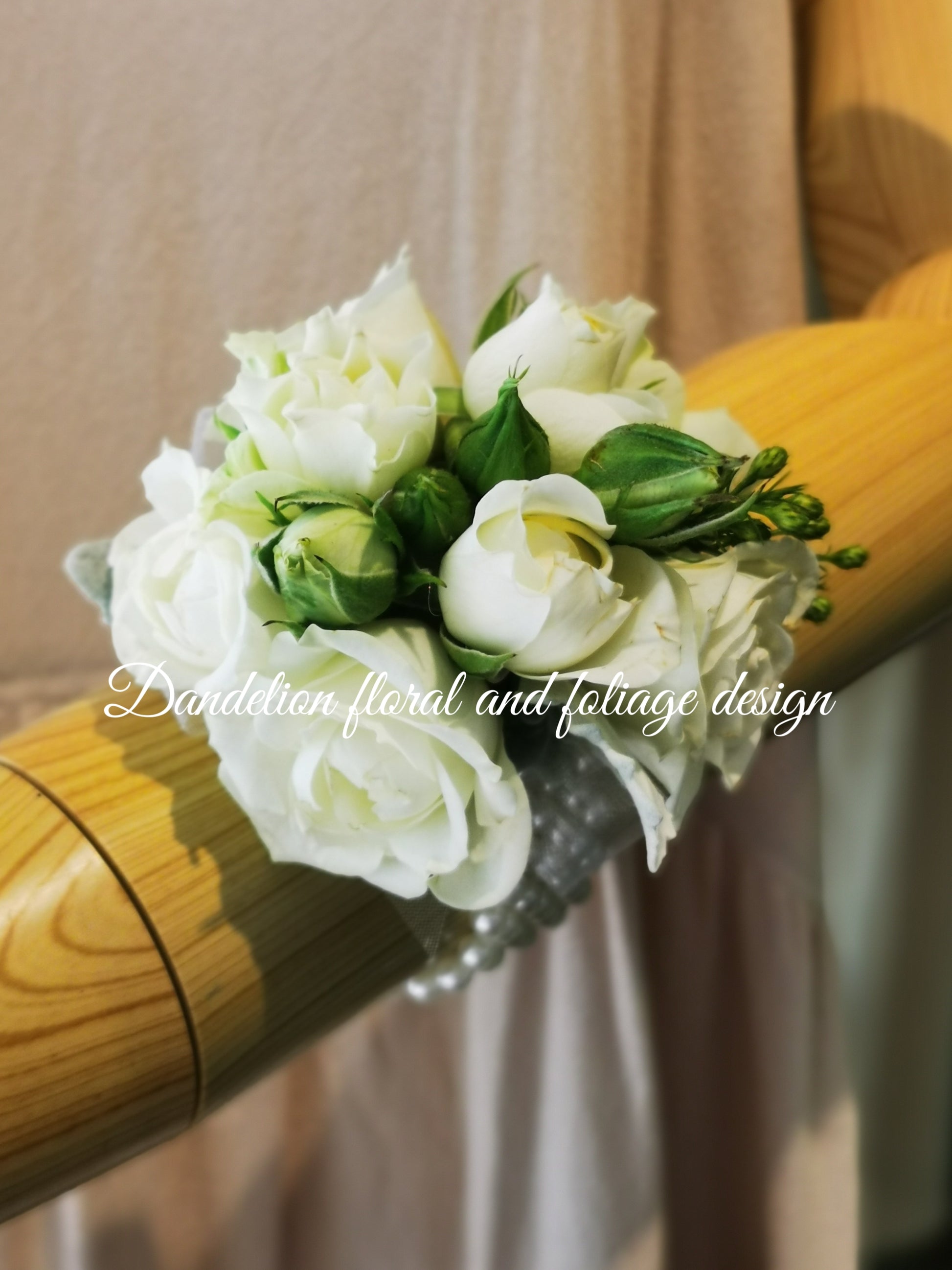 A wrist corsage featuring white flowers and green leaves, attached to a clear band.
